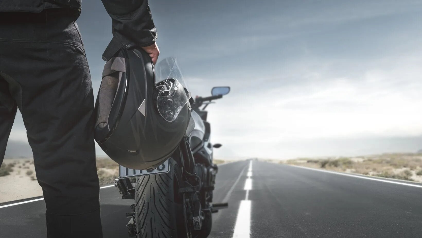 une personne qui se tient debout devant sa moto, avec un casque dans la main droite